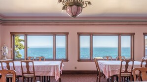 A dining area with tables and chairs, large windows with a view of the sea, and a chandelier. - Martine Inn (Pacific Grove)