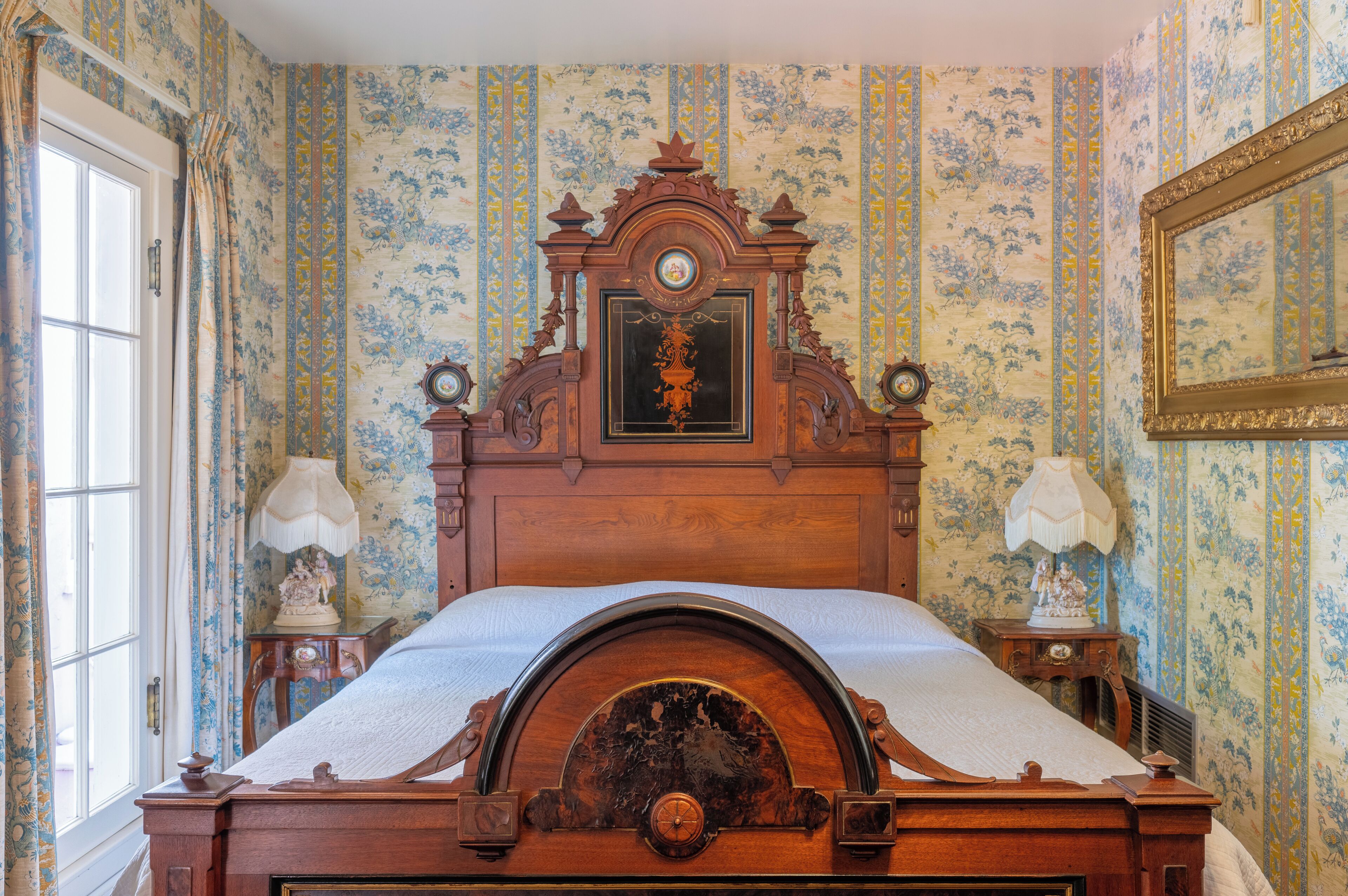 Une chambre à coucher avec un lit en bois, un papier peint à motifs floraux et deux tables de chevet avec des lampes.
