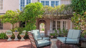 A patio area with outdoor seating, including chairs and tables, surrounded by greenery and a building in the background. - Martine Inn (Pacific Grove)