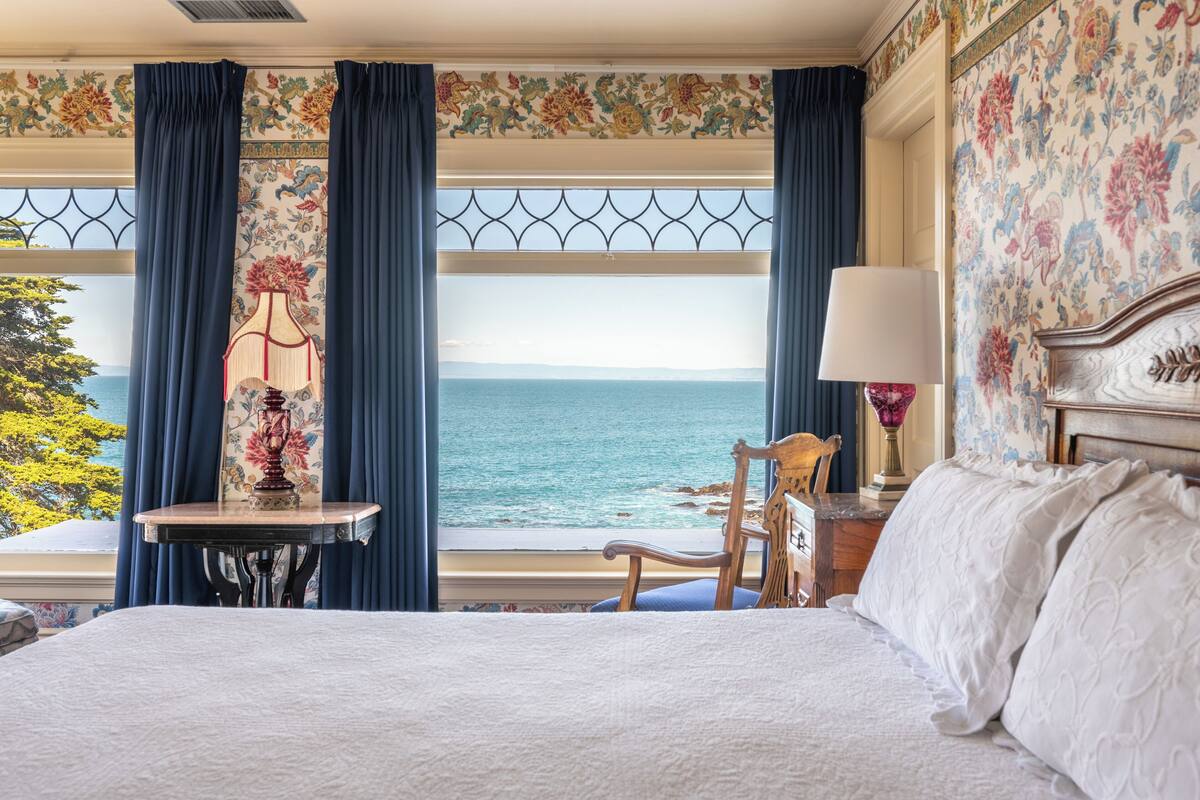 Ein Schlafzimmer mit einem großen Bett, einem Sessel, einem Tisch und Meerblick.