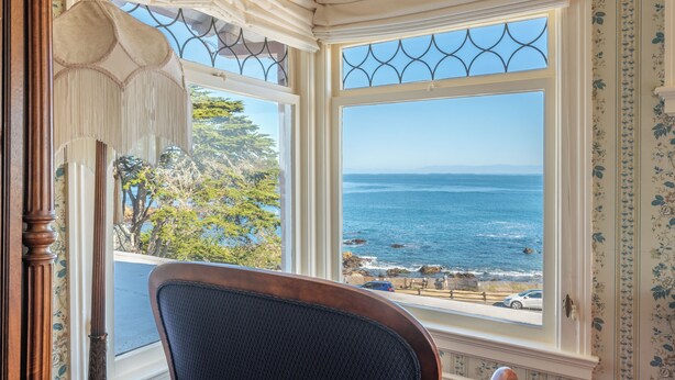 A room with a large window overlooking the ocean, a chair, and a decorative lamp. - Martine Inn (Pacific Grove)