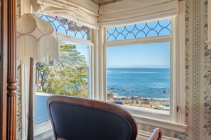 A room with a large window overlooking the ocean, a chair, and a decorative lamp. - Martine Inn (Pacific Grove)