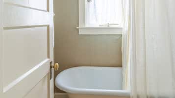 A bathroom with a white bathtub, a window with a white curtain, and a tiled floor.