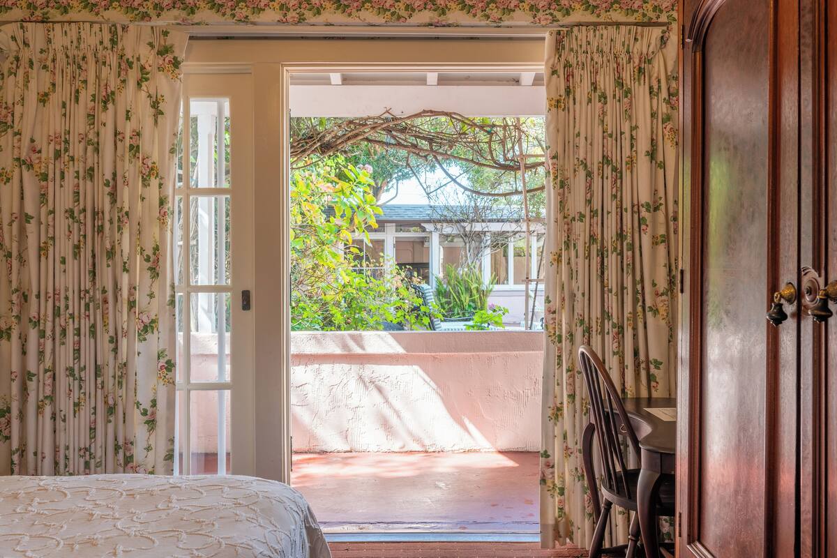 Ein Zimmer mit einem Bett, einer Holztür und Blick auf einen Garten durch eine geöffnete Tür.