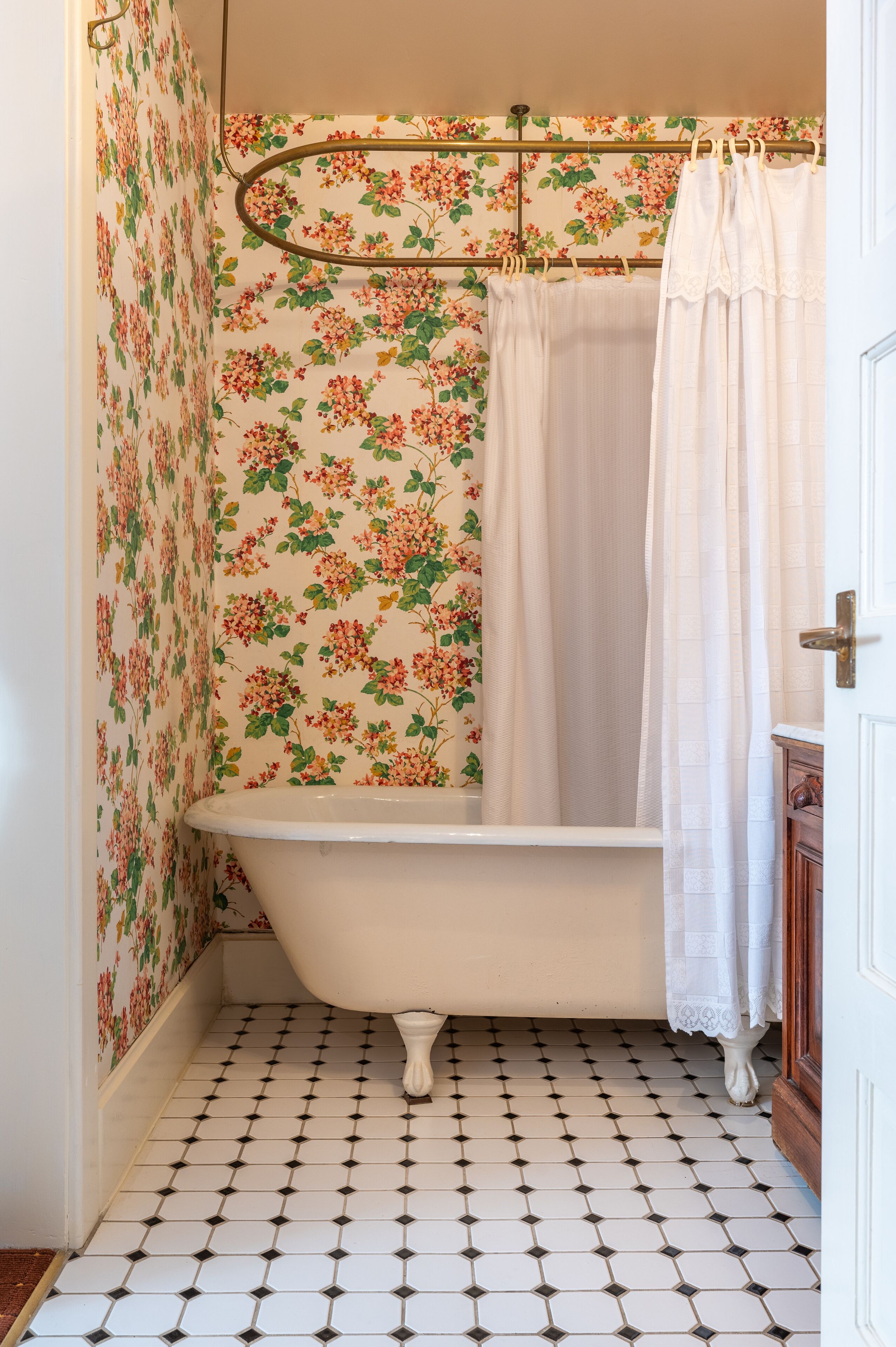 A bathroom with a clawfoot bathtub, floral wallpaper, and a tiled floor.