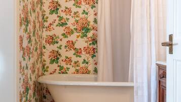 A bathroom with a clawfoot bathtub, floral wallpaper, and a tiled floor.