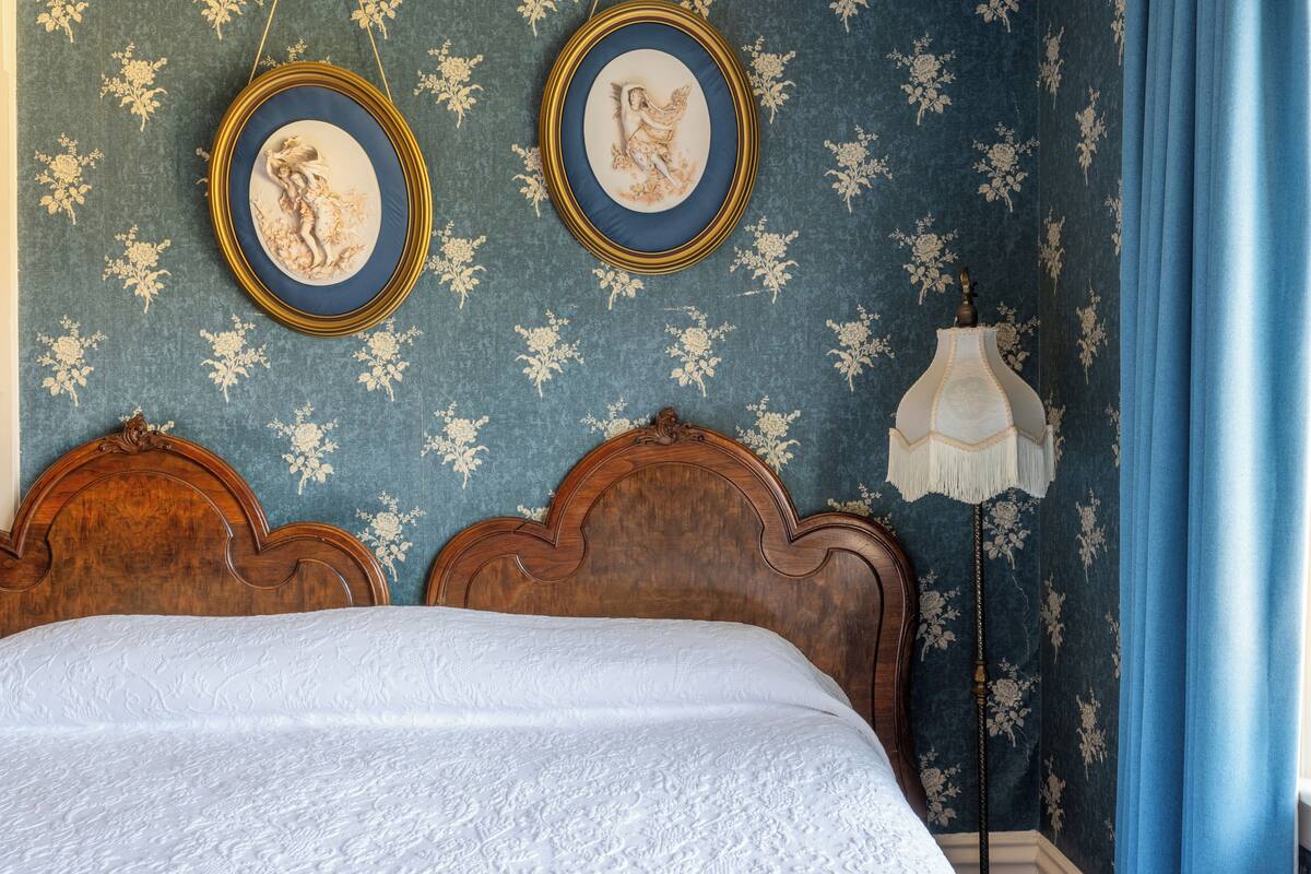 Ein Schlafzimmer mit einem hölzernen Bett, zwei gerahmten Wandbildern, einem Nachttisch und einer Lampe.
