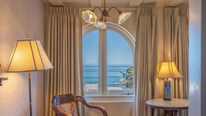 A room with a large arched window, a wooden chair, a small table with a lamp, and a floor lamp. - Martine Inn (Pacific Grove)