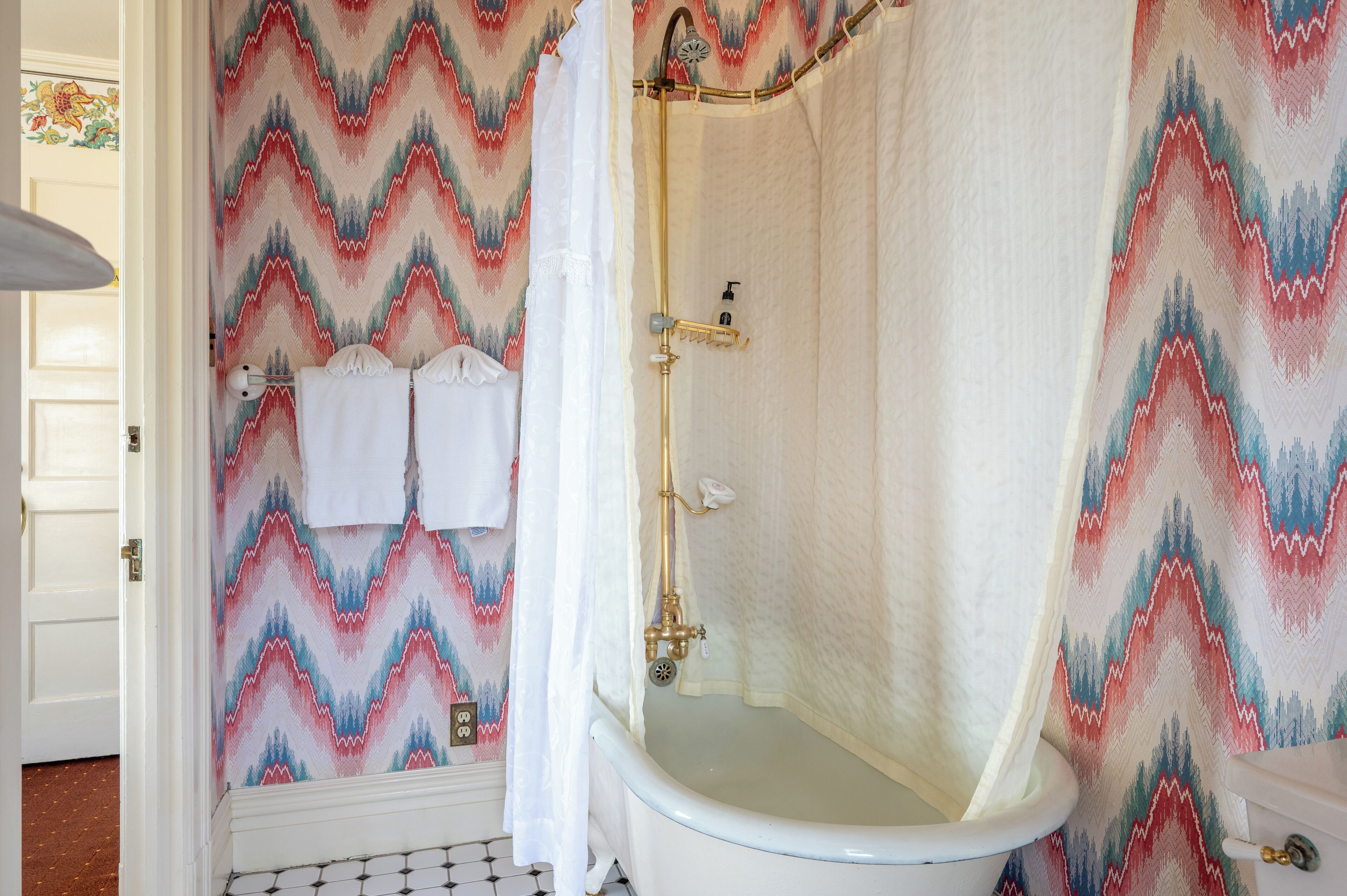 Un baño con bañera, cortina de ducha y papel tapiz estampado.