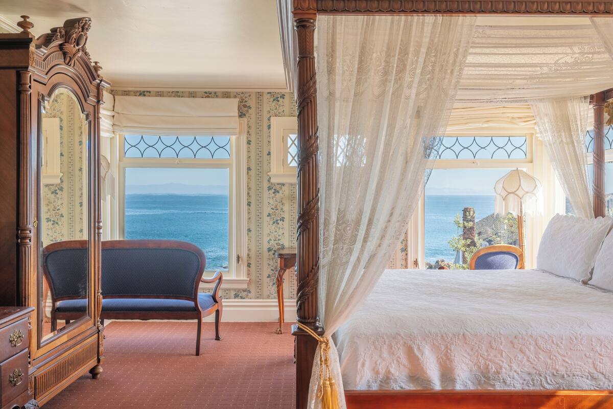 Ein Schlafzimmer mit einem großen Bett, einem Sessel, einem Schminktisch und Meerblick.