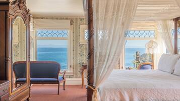 Un dormitorio con una cama grande, una silla, un tocador y vista al mar.