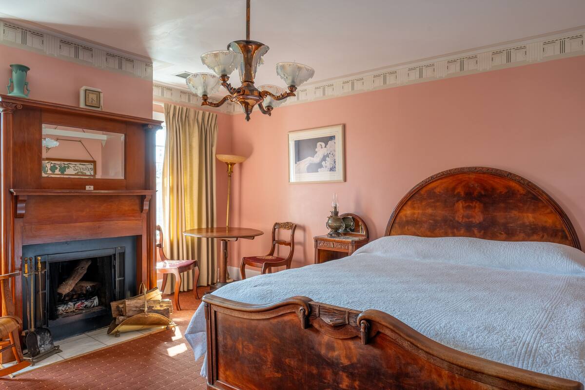 Ein Schlafzimmer mit einem großen Bett, einem Kamin, einer Kristallleuchter und einem gerahmten Bild an der Wand.