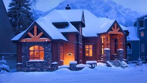 A snow-covered lodge with a stone facade, large windows, and a prominent chimney. - Buffaloberry B&B (Banff)