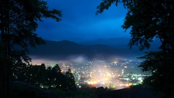 A nighttime view of a city with lights, surrounded by mountains and trees.