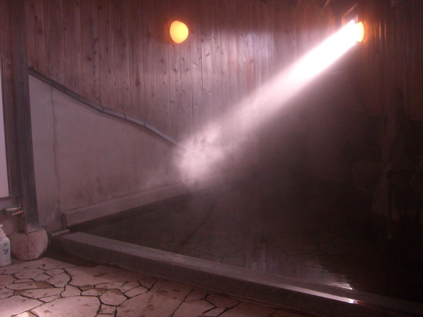 A steam room with a wooden interior, a stone floor, and a visible water pipe.