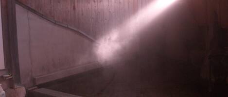 A steam room with a wooden interior, a stone floor, and a visible water pipe.