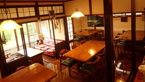 Ein traditionelles japanisches Restaurant mit Holztischen und -stühlen, einer roten Couch und großen Fenstern, die viel Tageslicht hereinlassen.