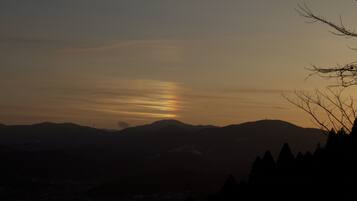 Un paysage de montagne au coucher du soleil, avec les silhouettes d’arbres et une ville en contrebas.