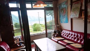 Ein Zimmer mit einem roten Ledersofa, einem Holztisch und Blick auf Berge durch große Fenster.