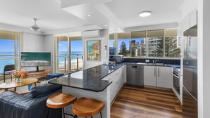 A modern kitchen with a large island, bar stools, and a view of the ocean. - Viscount on the Beach (Surfers Paradise)