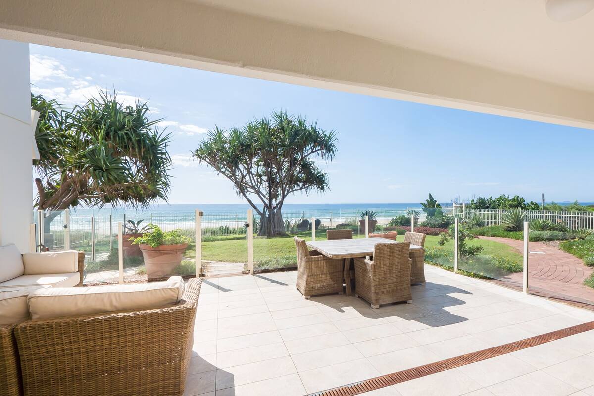 A balcony with a view of the beach, wicker furniture, and potted plants.