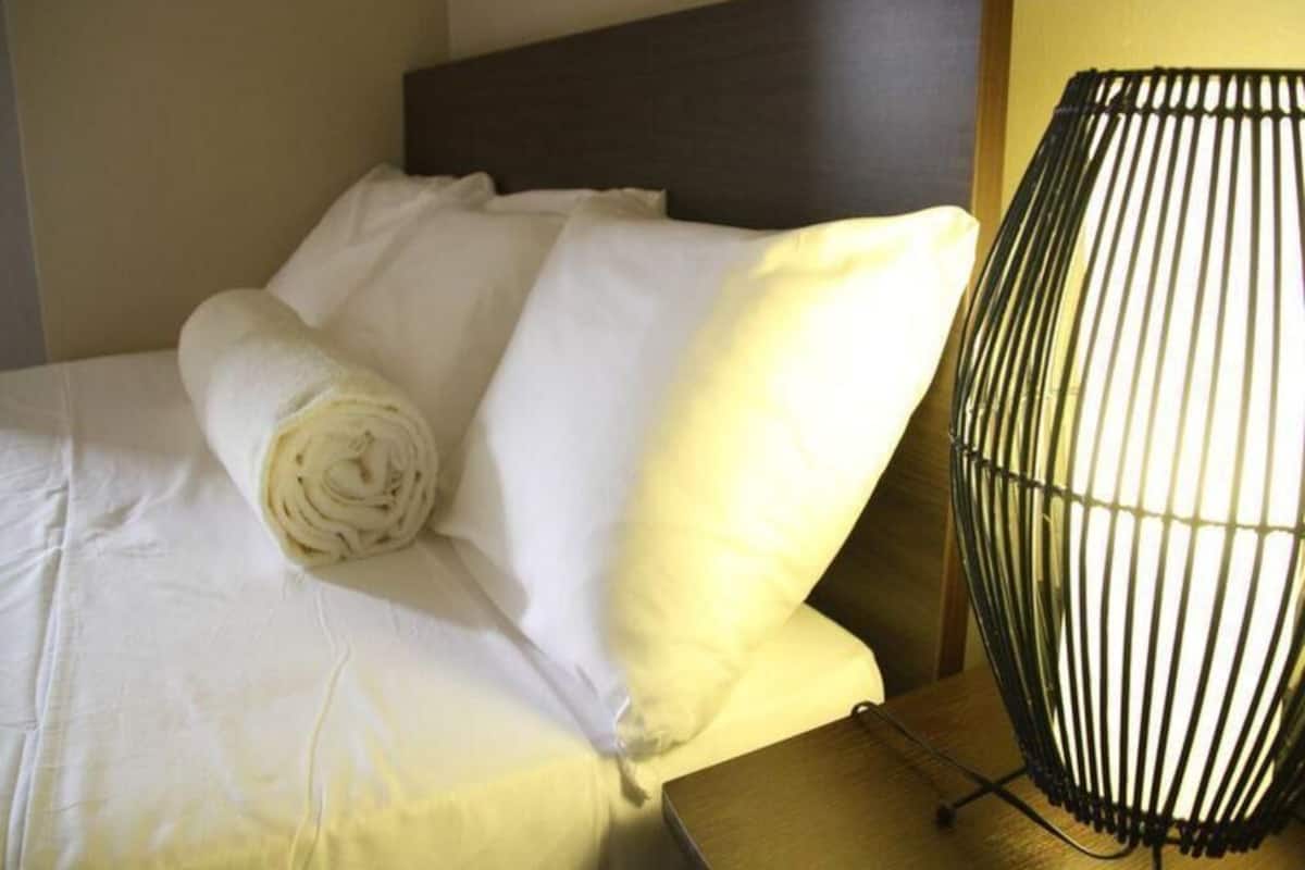 A neatly made bed with white linens, a rolled towel, and a black metal lamp on a wooden nightstand.