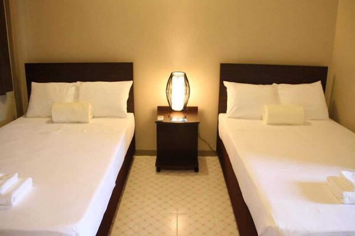 A hotel room with two beds, a nightstand with a lamp, and a carpeted floor.