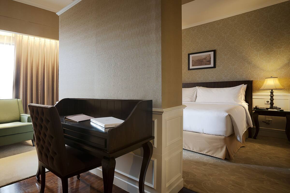 A hotel room with a green sofa, a piano, a bed, and a desk with a lamp.