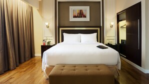 A hotel room with a large bed, a nightstand, a bedside table, a mirror, and a window with curtains. - Royal Kuningan Hotel (Jakarta)