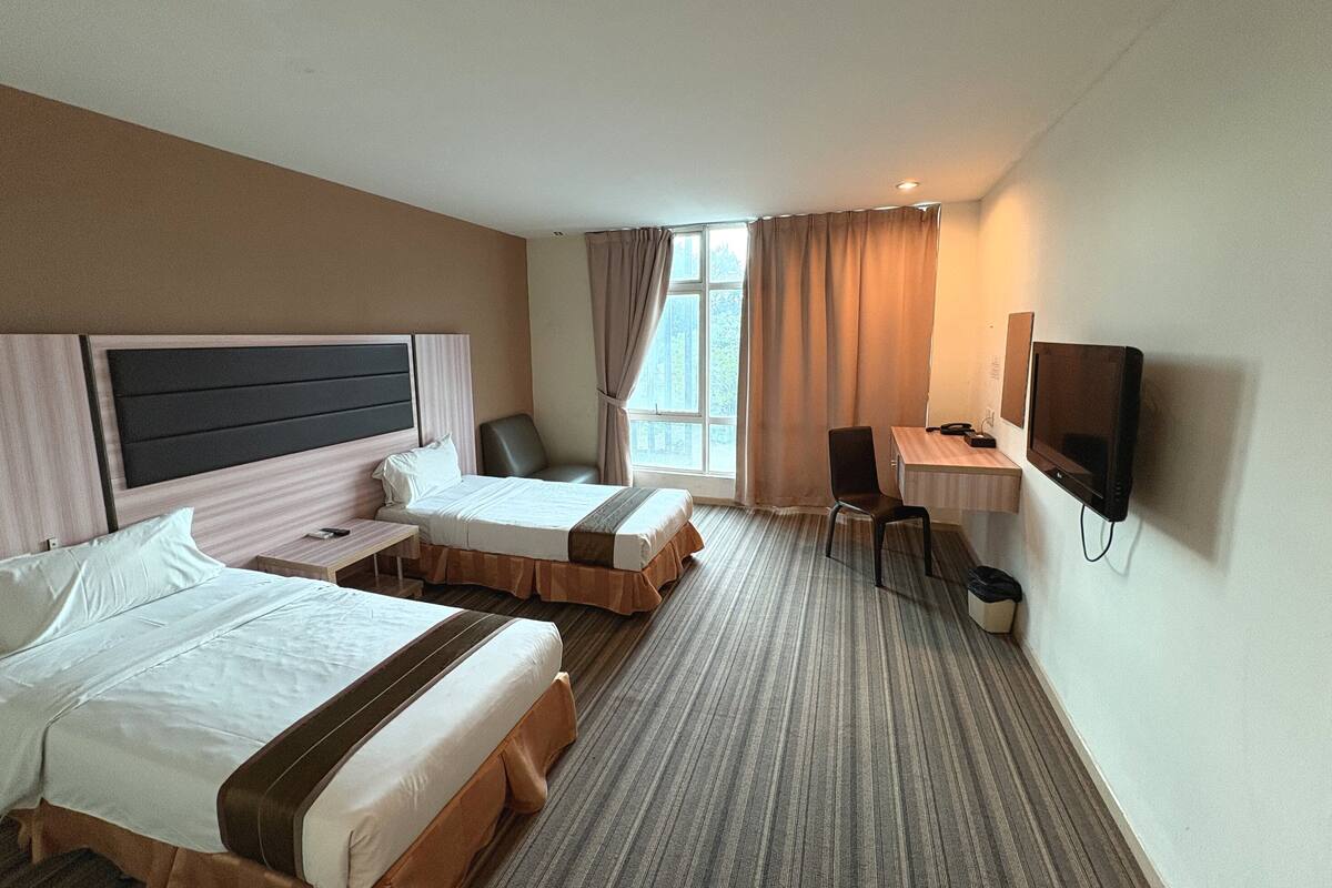 Ein Hotelzimmer mit zwei Betten, einem Schreibtisch, einem Sessel, einem Fernseher und einem Fenster mit Vorhängen.