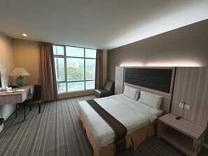 Une chambre d’hôtel avec une grande fenêtre, un lit, un bureau avec une lampe et une chaise.