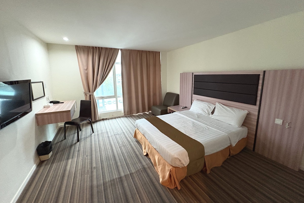 Ein Hotelzimmer mit Bett, Schreibtisch, Stuhl, Fernseher und einem Fenster mit Vorhängen.