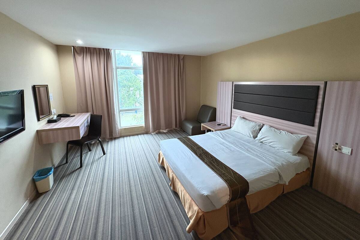 Ein Hotelzimmer mit Bett, Schreibtisch, Stuhl, Fernseher und einem Fenster mit Vorhängen.