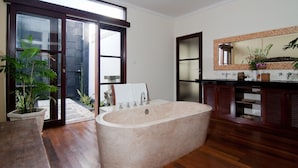 Un baño con una bañera independiente grande, un tocador de madera, un espejo y una planta en maceta.