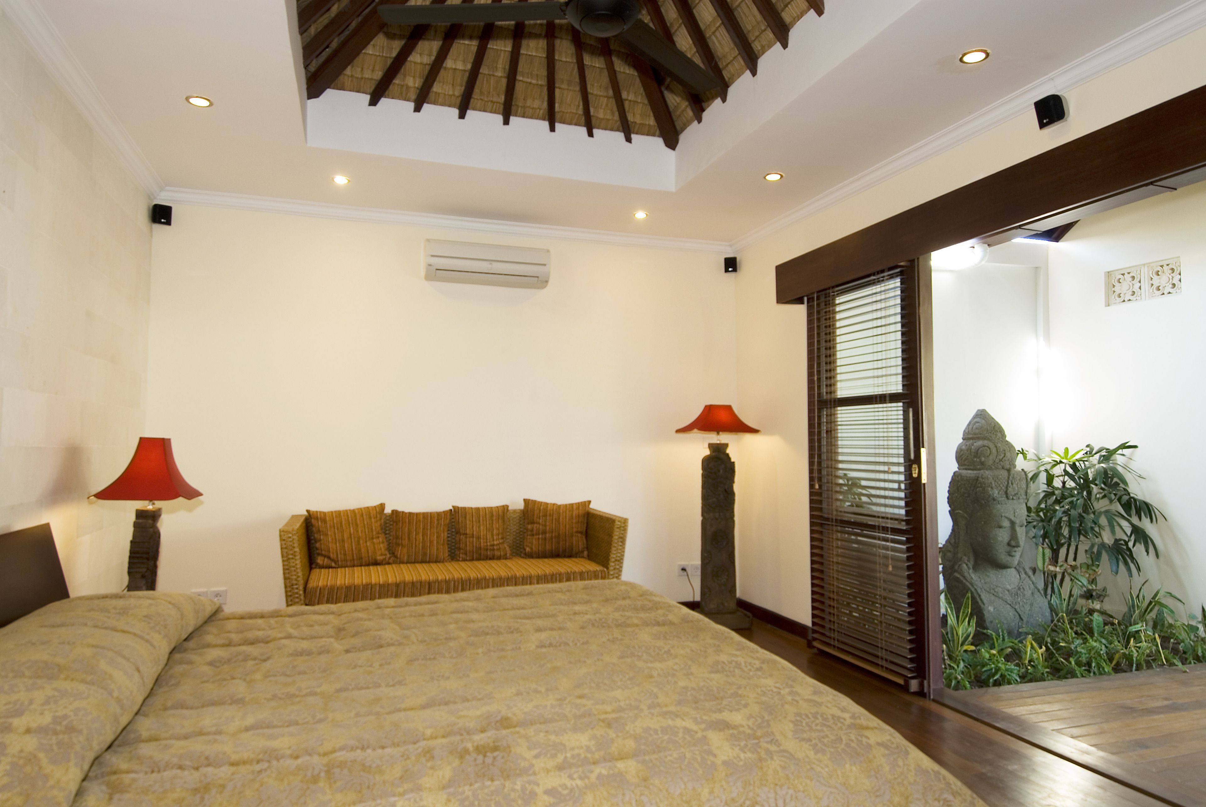 Un dormitorio con cama, sofá, lámpara roja, aire acondicionado y una estatua.