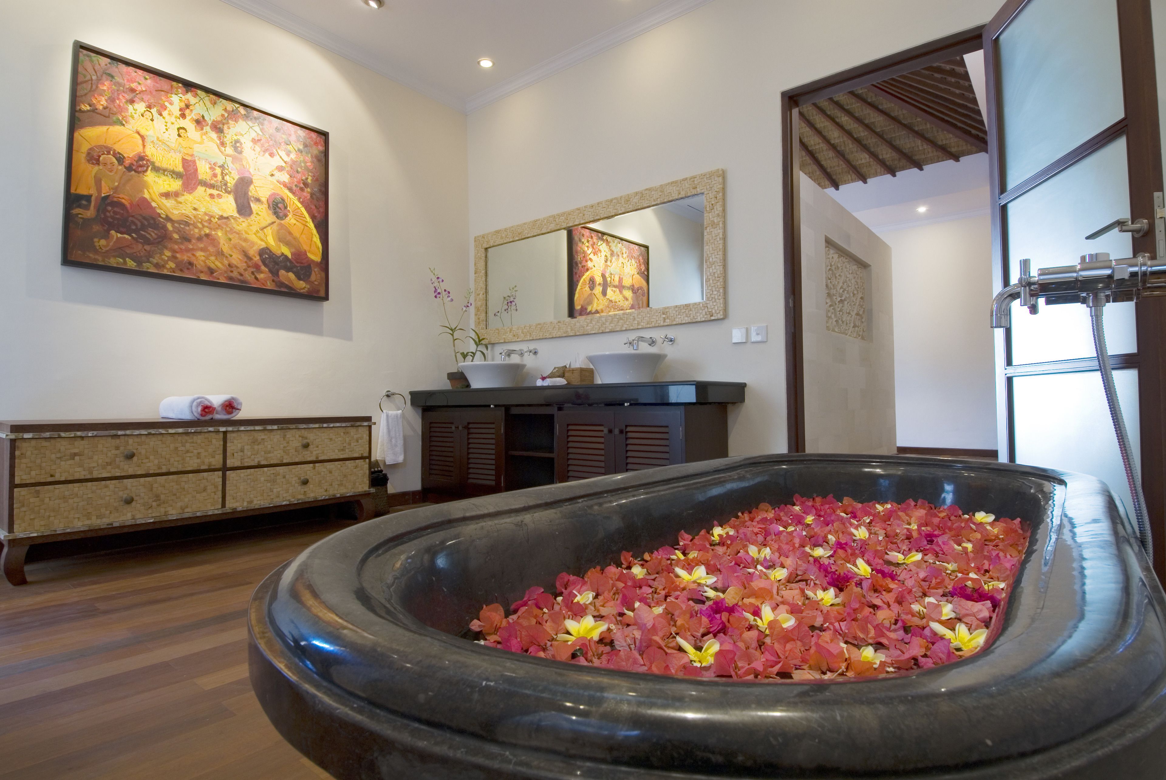 A spa area with a large stone basin filled with flower petals, a wooden cabinet, a sink, and a large mirror on the wall.