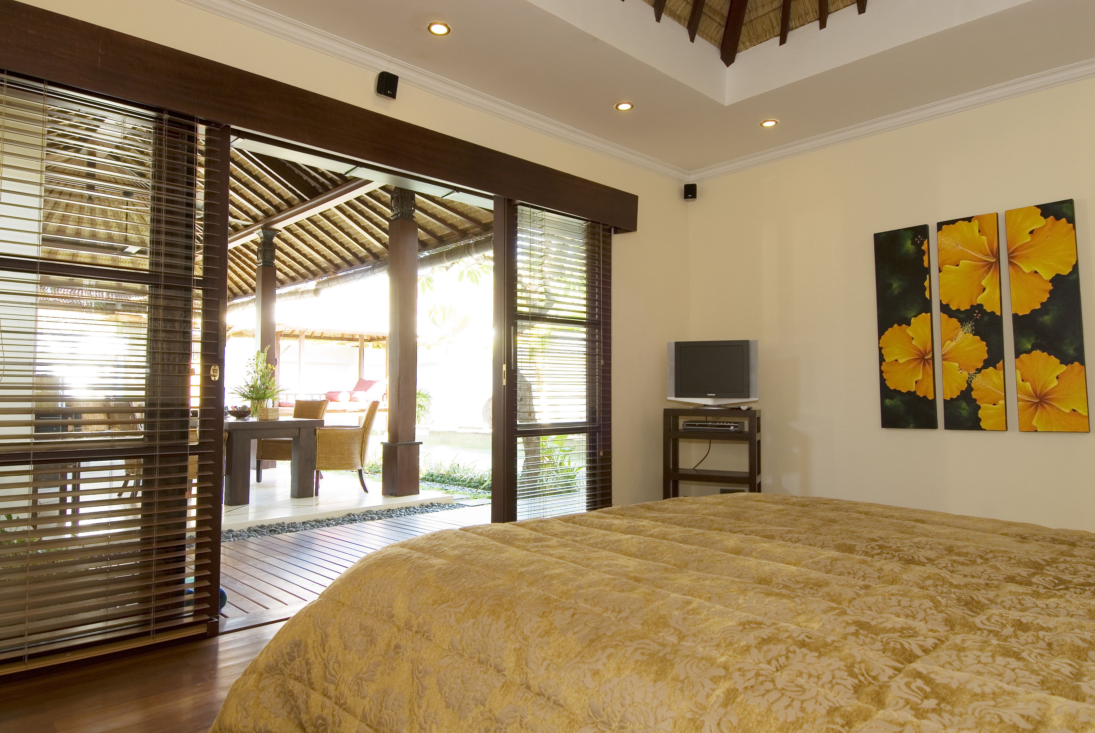 Ein Schlafzimmer mit einem großen Bett, einem Fernseher und Blick auf einen Außenbereich mit Tisch und Stühlen.