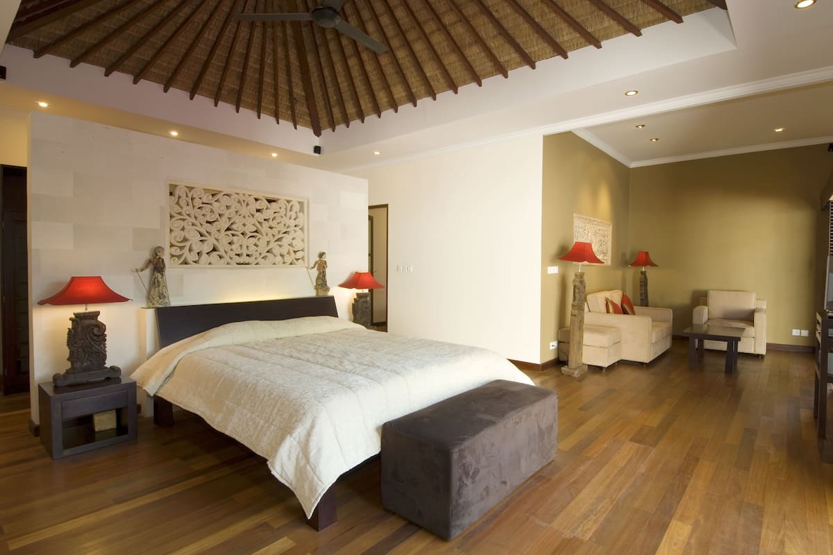 Une chambre spacieuse avec un grand lit, un plafond en bois et un coin salon comprenant deux fauteuils.