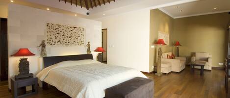 Een ruime slaapkamer met een groot bed, een houten plafond en een zithoek met twee stoelen.