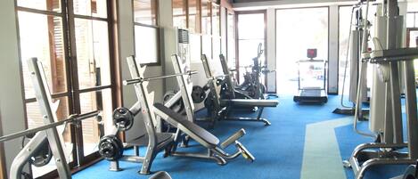 A gym with various exercise equipment, large windows, and a blue carpeted floor.