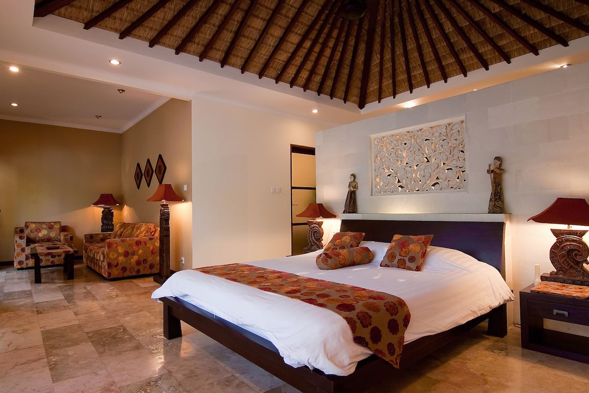 Une chambre spacieuse avec un grand lit, un coin salon comprenant un canapé et des fauteuils, et un élément décoratif mural.