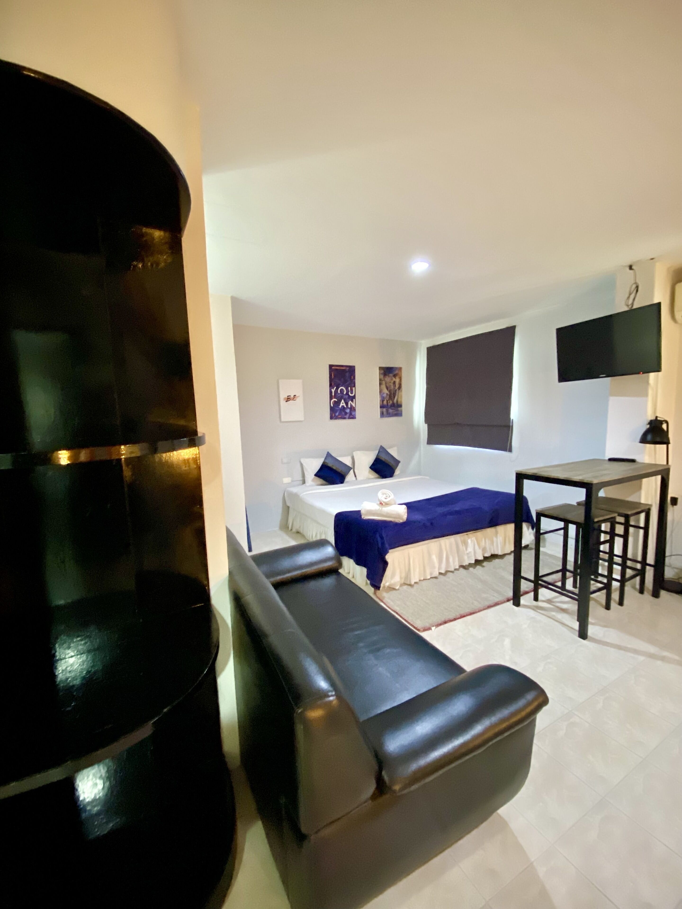 A hotel room with a bed, a desk, a chair, a TV, and a large black cylindrical object.