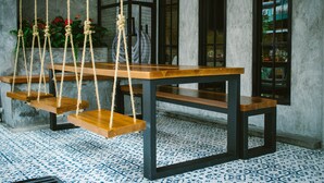 A wooden table with rope swings, a patterned floor, and a window with a view of the outside. - BH Baan Paradise (Patong)