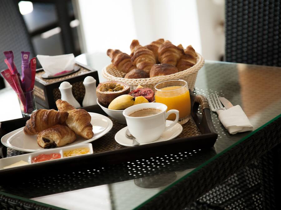 Ein Frühstücksbrett mit Croissants, Obst, Kaffee und Orangensaft auf einem Glastisch.