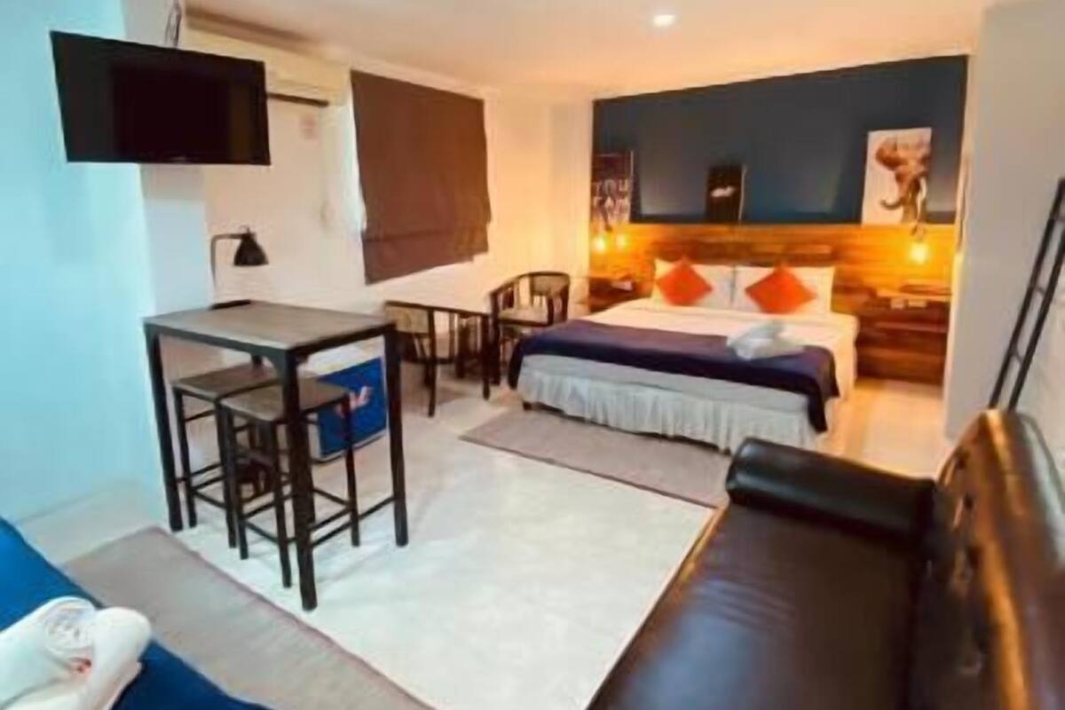 Un espacio habitable compacto con sofá, cama, escritorio y televisor instalado en la pared.