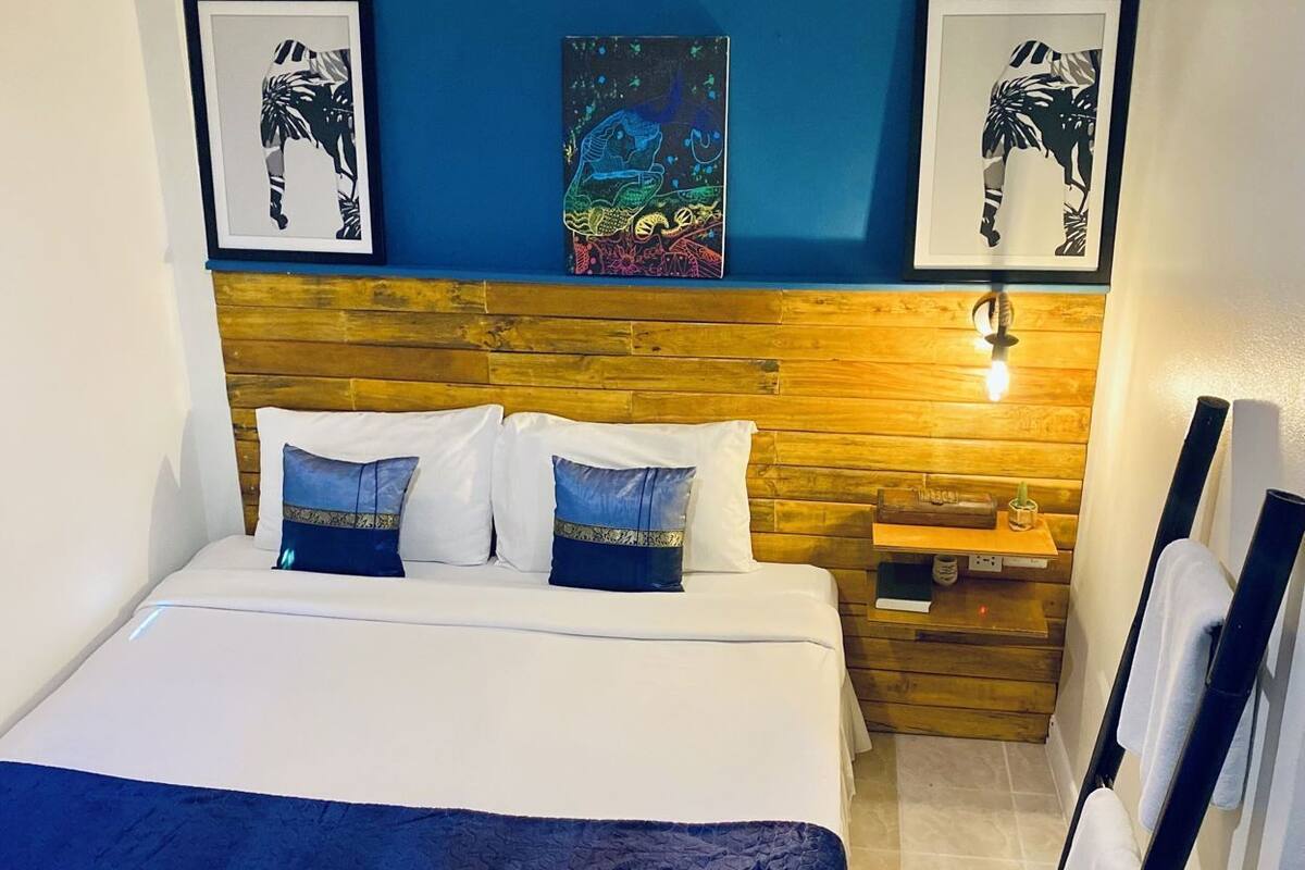 Una habitación de hotel con cama, cabecero de madera, obras de arte en las paredes y una mesita de noche.
