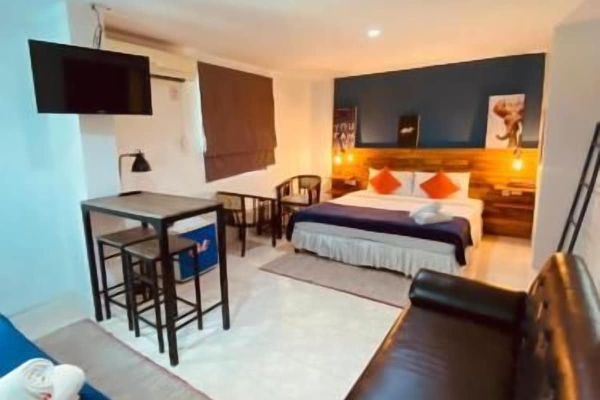 Un espacio habitable compacto con sofá, cama, escritorio y televisor instalado en la pared.