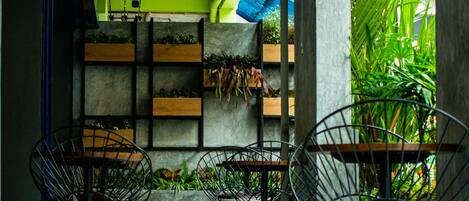 A covered outdoor seating area with metal chairs and tables, surrounded by planters with greenery.