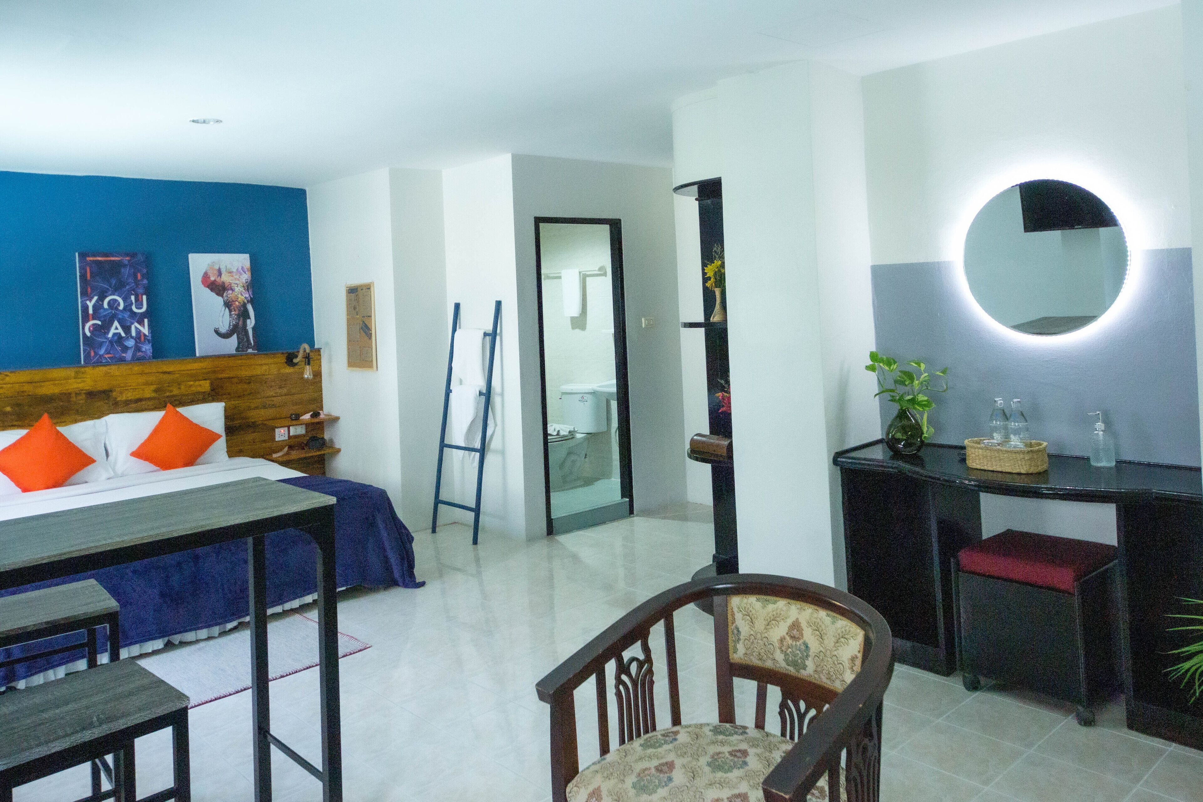 A hotel room with a bed, a desk, a chair, a mirror, and a bathroom visible through an open door.