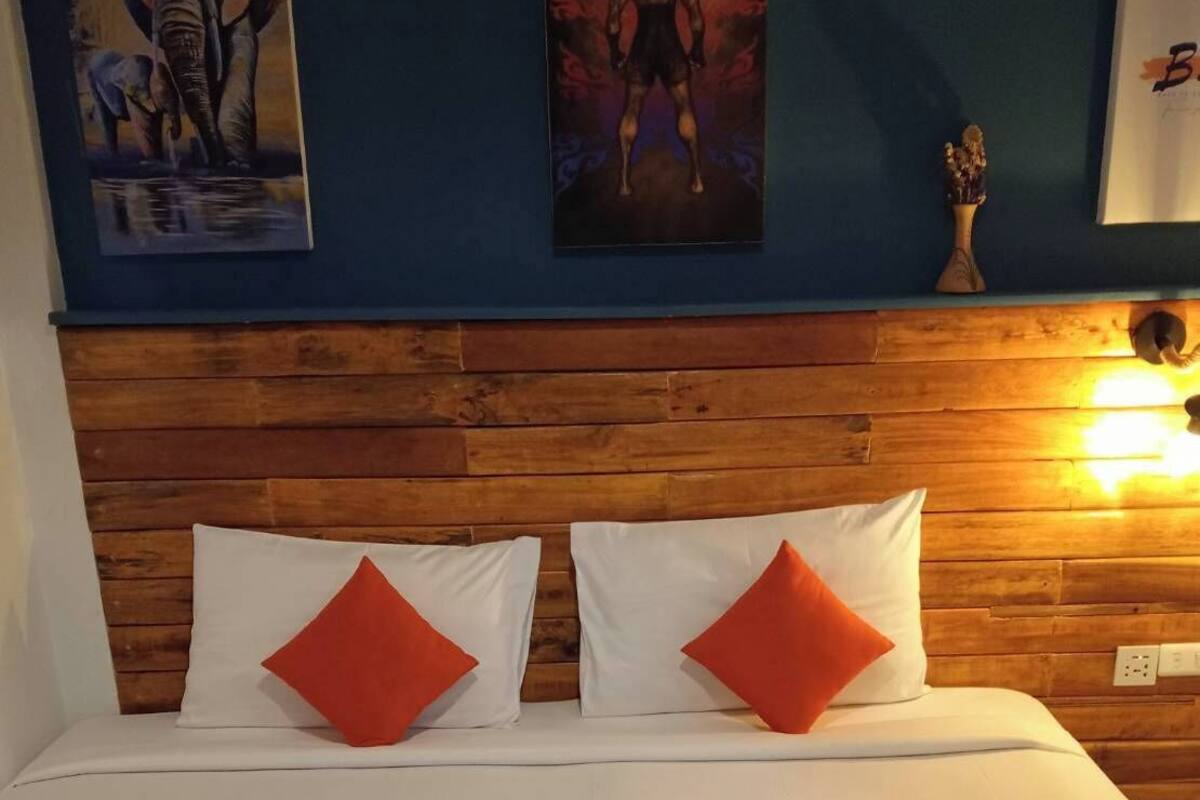 Habitación de hotel con cabecera de madera, ropa de cama blanca, almohadas rojas y una manta azul con toallas.